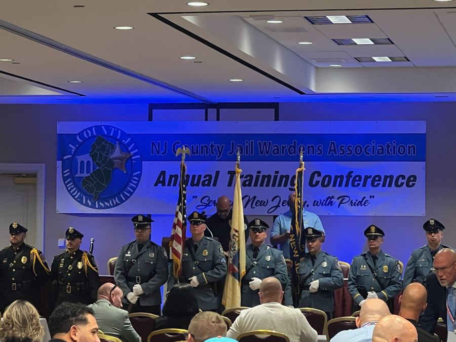 Uniformed color guard with flags standing before the NJ County Jail Wardens Association Annual Training Conference banner