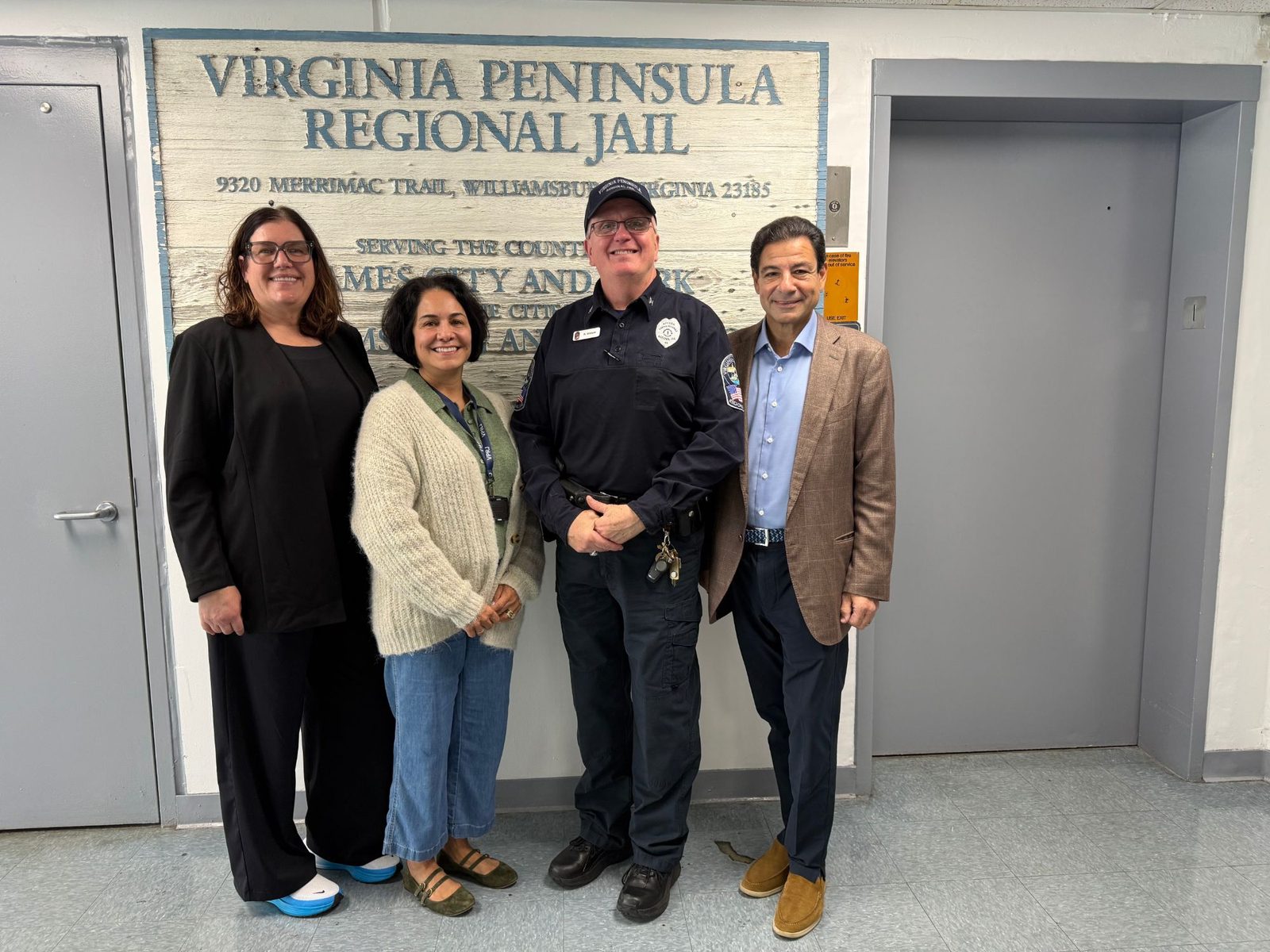 Four people smiling in front of the Virginia Peninsula Regional Jail sign, with Superintendent Roy Witham in uniform between members of the CBH Medical team
